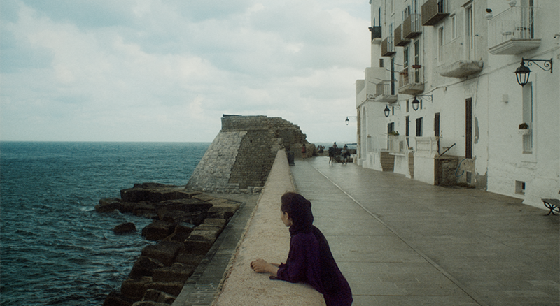 Woman leaning on a wall by the sea in Italy